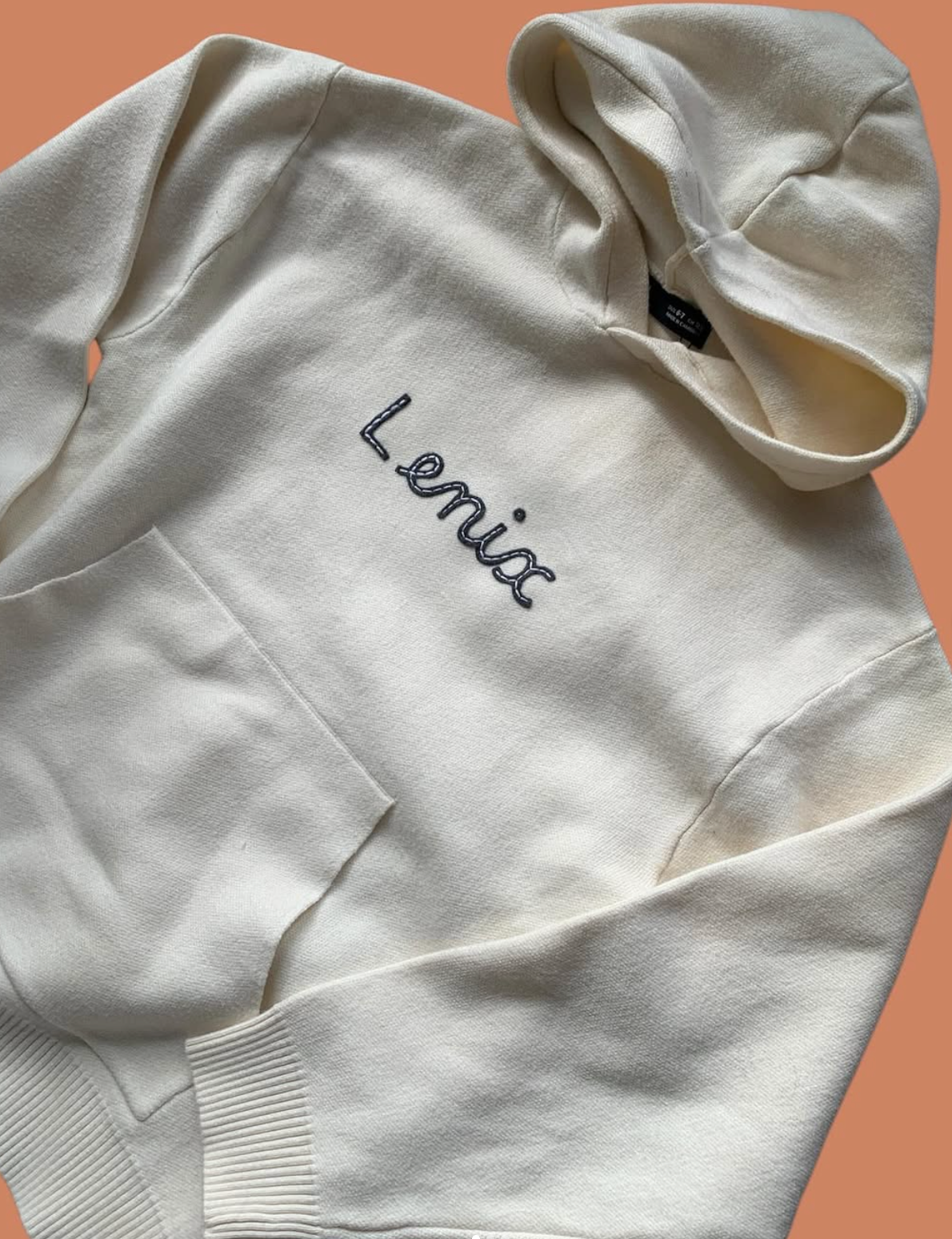 White hoodie with 'Lenia' embroidery on a peach background